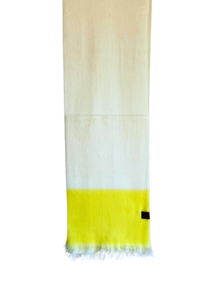 A lightweight woven scarf in white and bright yellow, hanging from a wooden hanger against a plain white background. The scarf features a small black square label near the bottom right corner.