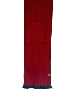 A dark red wool scarf with a blue ombre gradient at the bottom fringe, hanging from a wooden hanger against a white background.